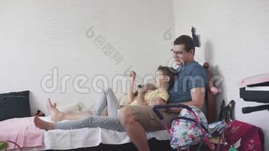 一个年轻的父亲和他的小女儿在一起。 爸爸和孩子在家坐在床上玩。 亲子